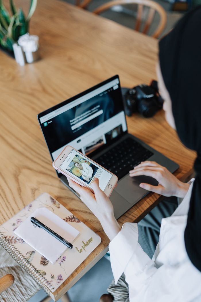 Young woman using a smartphone and laptop, representing modern technology multitasking.